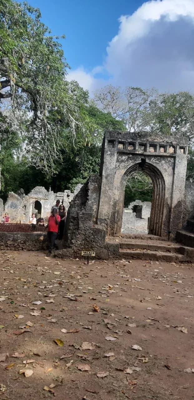 The stone arch at the entrance to a historic site, with visitors under the trees.