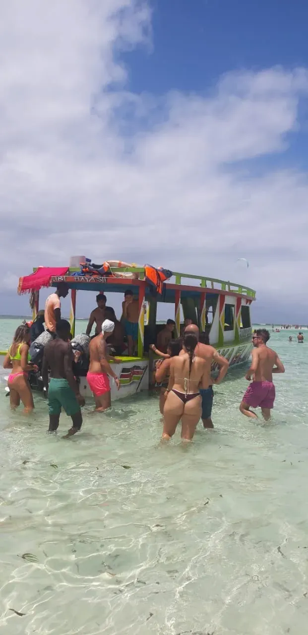 Os hóspedes em pé nos rasos ao lado do barco de excursão.