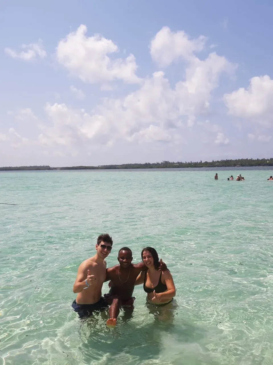 Drei Gäste hüfttief im türkisfarbenen Wasser, niedrige Wolken am Horizont.