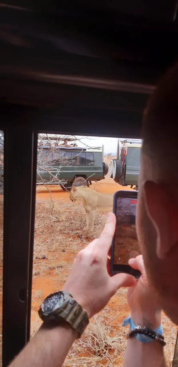A guest taking a photo with their phone from the open door of the safari vehicle, stopped on the red track.