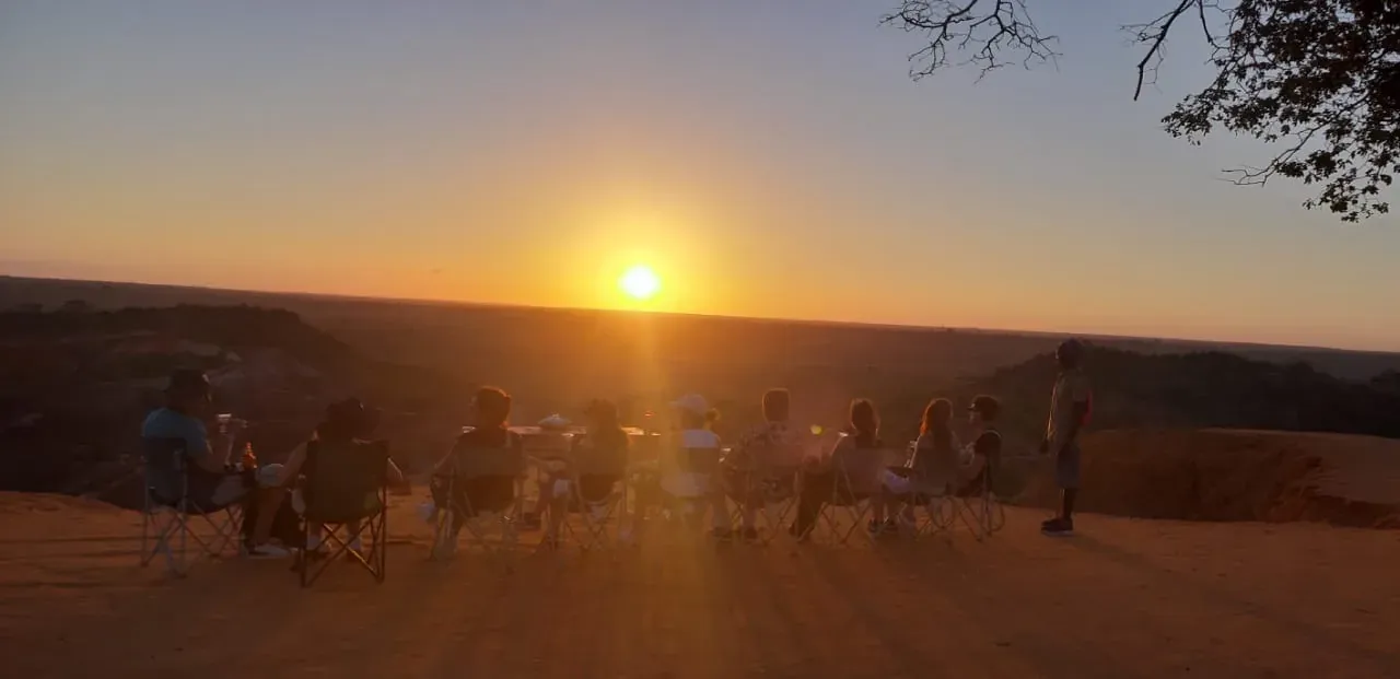 De groep gasten die op rij op de bergkam zitten, kijkend naar de zonsondergang.